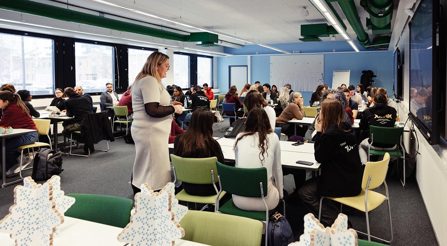 Lecturer in a middle of classroom full of students.